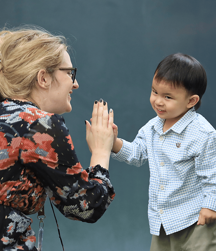  Bright Start toddler giving a high five to the teacher at Brighton College Bangkok Vibhavadi, celebrating joyful learning and warm teacher–child connection. 